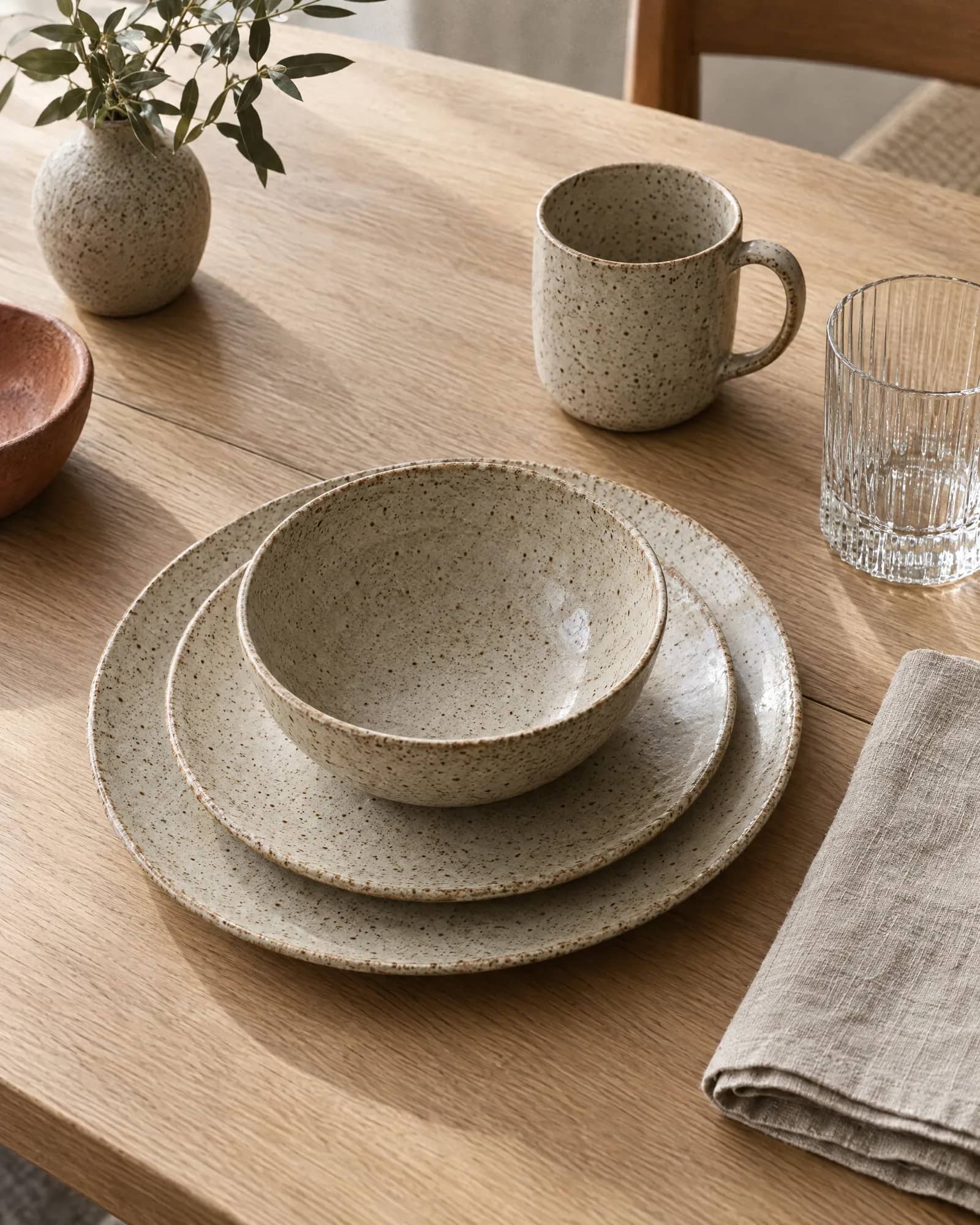 Speckled stoneware place setting with a ribbed glass on an oak table