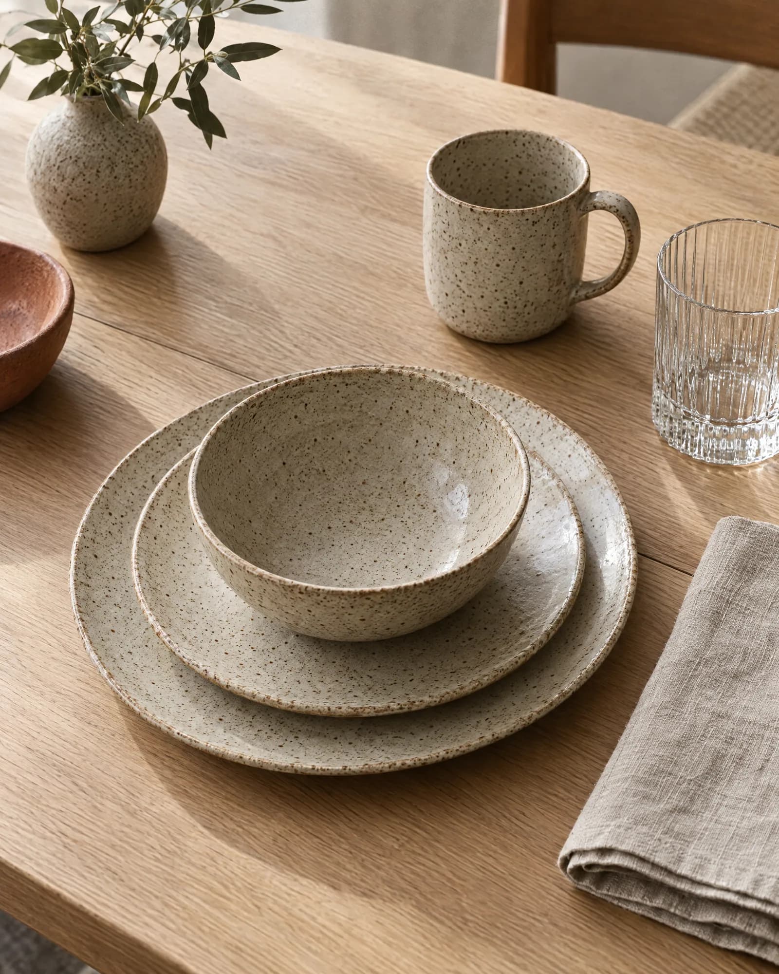 Speckled stoneware place setting with a ribbed glass on an oak table